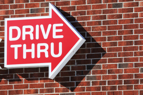Drive-thru sign on brick wall hinting California fast food minimum wage increase 2024